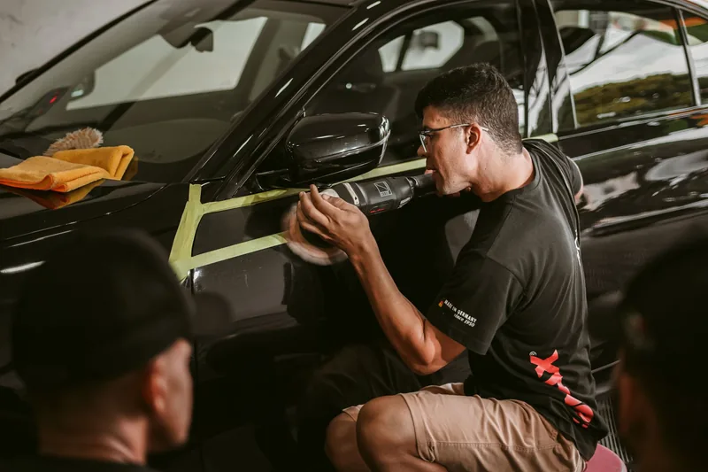 Car detailer machine-polishing the door of a dark car