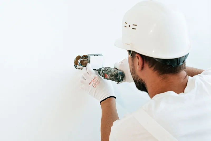 Handyman in a hard hat fixing a switch on a wall