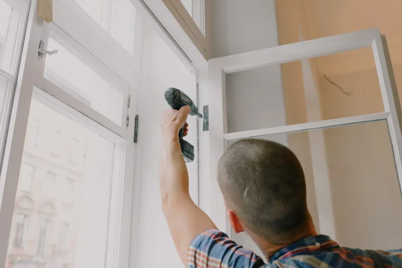 Handyman installing a window frame with a cordless drill