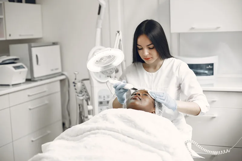 Aesthetician performing a facial under a treatment lamp