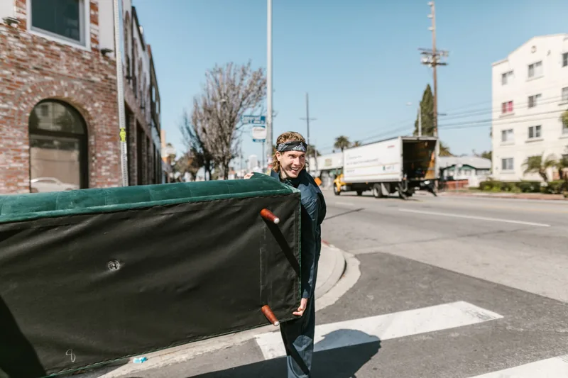Mover carrying a couch across a sunny street