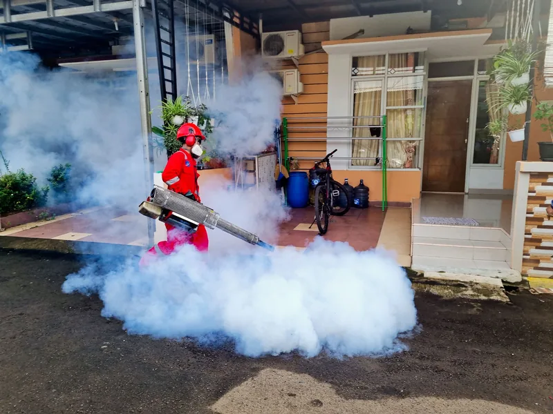 Pest control specialist fogging the outside of a house